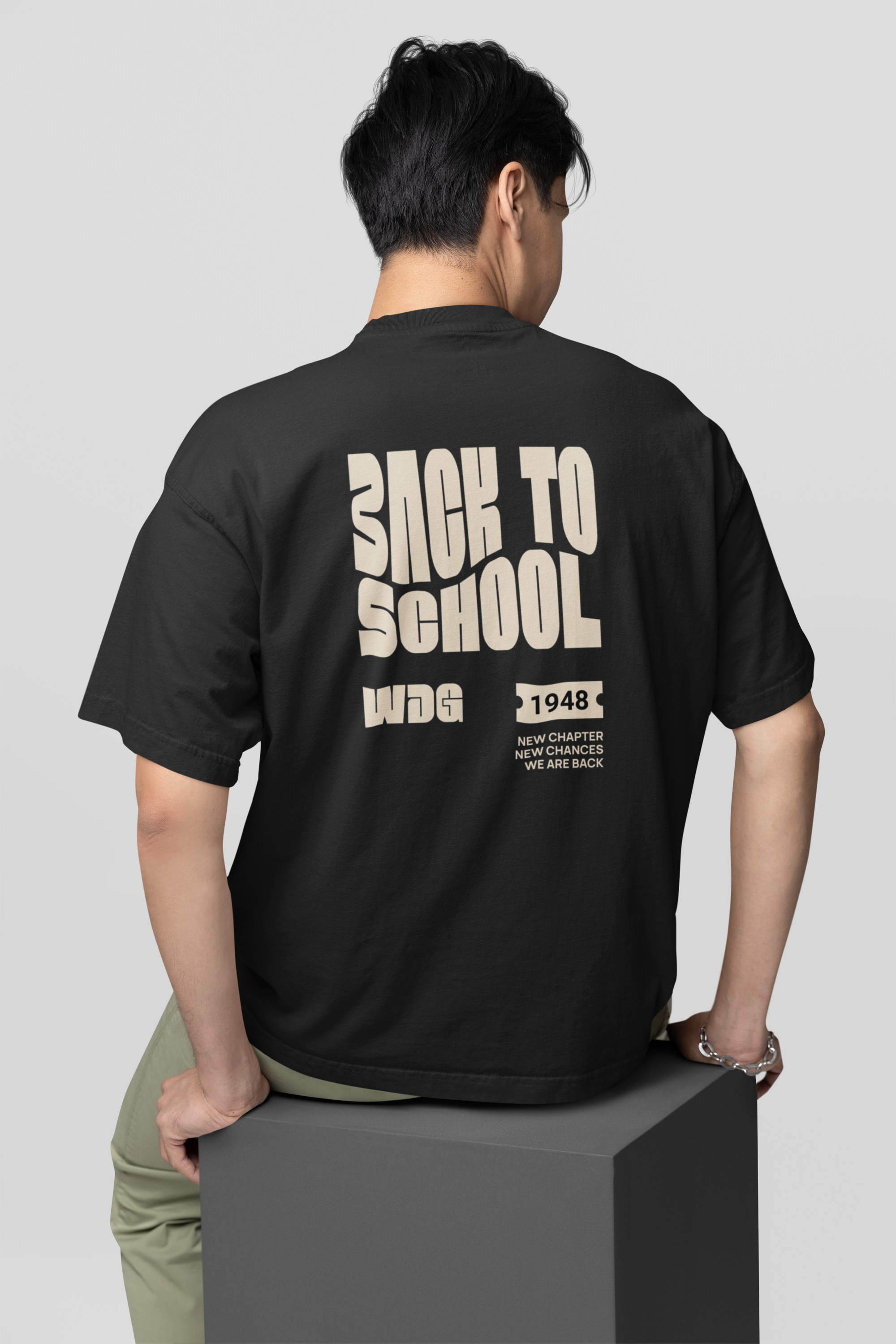 Ein Schüler von hinten trägt ein oversized schwarzes T-Shirt mit großem, cremefarbenem Text auf dem Rücken, der 'BACK TO SCHOOL', sowie kleinere Details zeigt.